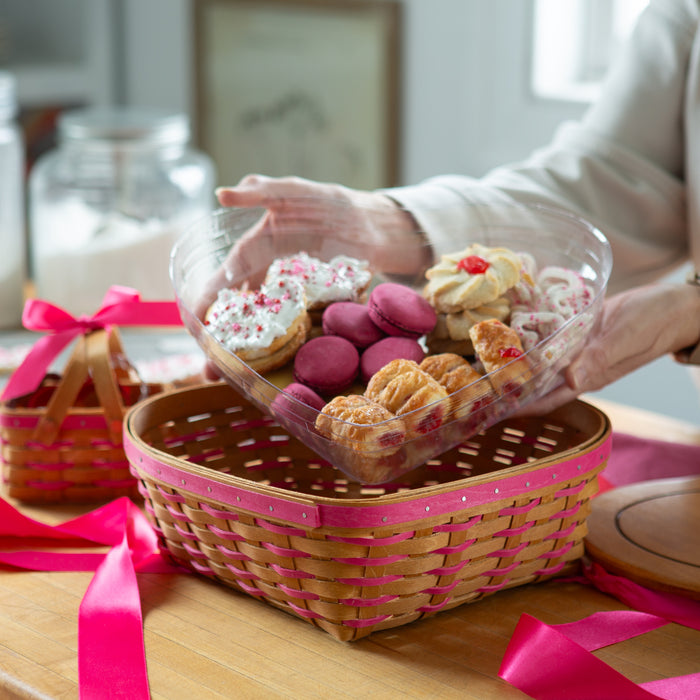 Person holding a transparent container with pastries over a pink Longaberger basket on a table.