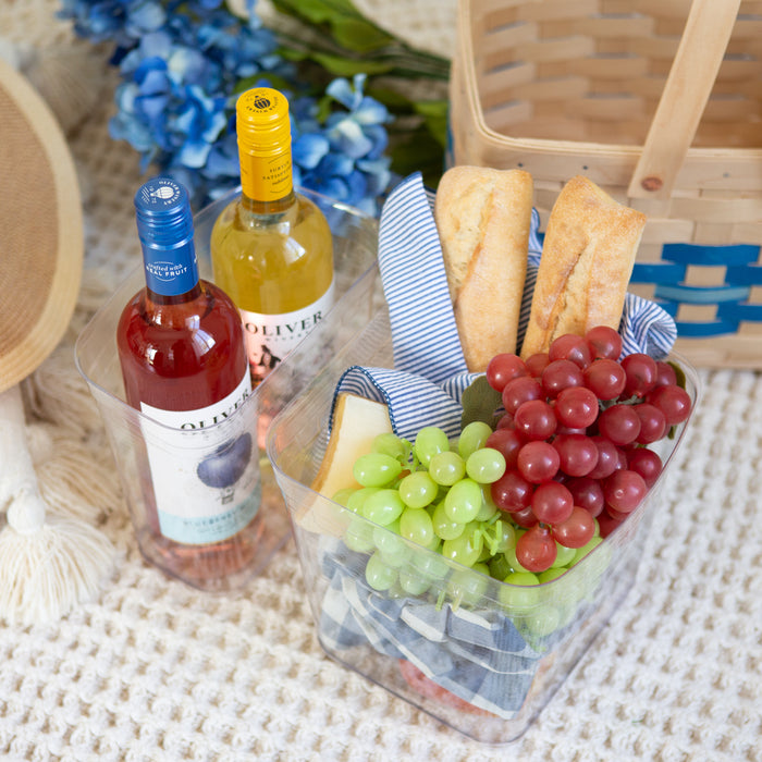 Fruit basket with grapes, apples, and a bottle of wine on a textured surface.