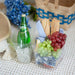 Picnic setup with Perrier bottle, grapes, bread, and cheese on a blanket.